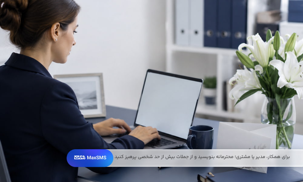 فردی در محیط اداری در حال نوشتن پیام رسمی تسلیت با لپ‌تاپ، کارت ساده و گل‌های سفید 